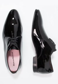 Chaussures habillées en cuir verni noir avec un bout pointu, des lacets et une texture lisse ; elles présentent une semelle intérieure rose avec le logo "Floris van Bommel".