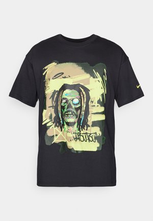 T-shirt de algodão preta com uma impressão gráfica colorida de um crânio com óculos de sol e elementos de grafite em tons de verde e amarelo.