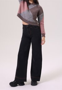 Pull crochet avec un design court en nuances de rose, gris et marron, associé à un jean noir taille haute à jambes larges et des baskets noires épaisses.