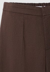 Pantaloni marroni con tessuto testurizzato, dotati di vita sagomata e piega frontale, progettati per una vestibilità slim senza tasche visibili.