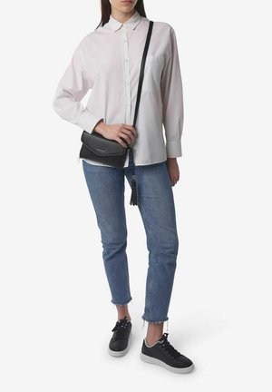 Camisa blanca de manga larga, fabricada en un material ligero, con botones frontales, combinada con pantalones vaqueros azules, zapatillas negras y un pequeño bolso negro tipo bandolera con un fleco.