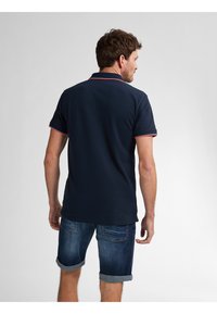 Námořnicky modré polo tričko s červenými akcenty na límci a rukávech, spárované s ohrnutými džínovými šortkami. Hladká tkanina a neformální design.