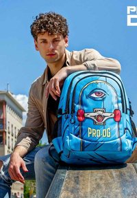 Mochila azul con diseño de ojos de dibujos animados, acentos rojos en el hardware y texto en negrita "PRO-DG". Tejido texturizado con compartimentos con cremallera y lados de malla.