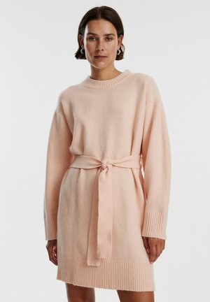 Helles rosa Strickkleid mit geripptem Saum und Bündchen. Mit einem Bindegürtel in der Taille, der eine lässige Silhouette schafft. Weicher Stoff.