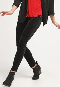 Černé slim-fit kalhoty vyrobené z měkké tkaniny, zkombinované s červenou blůzou a černými botami na podpatku do kotníků se zipovým uzávěrem.