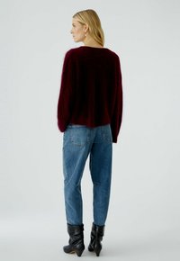 Bordeaux gebreide trui met een losse pasvorm en lange mouwen, gecombineerd met hoge taille blauwe jeans en zwarte enkellaarzen met een opgevouwen schacht.