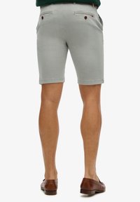 Lichtgrijze shorts met een gladde textuur, voorzien van twee achterzakken met bruin knopen en een opgerolde zoom bij de benen.