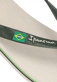 Chancla verde de goma con una correa texturizada que presenta un emblema de la bandera brasileña, y una plantilla blanca acolchada con un borde verde.