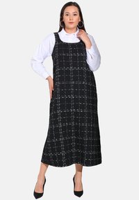 Robe midi à carreaux noir et blanc avec un décolleté carré, de fines bretelles et une coupe décontractée, portée sur une chemise à manches longues blanche.