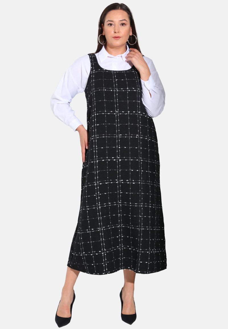 Robe midi à carreaux noir et blanc avec un décolleté carré, de fines bretelles et une coupe décontractée, portée sur une chemise à manches longues blanche.