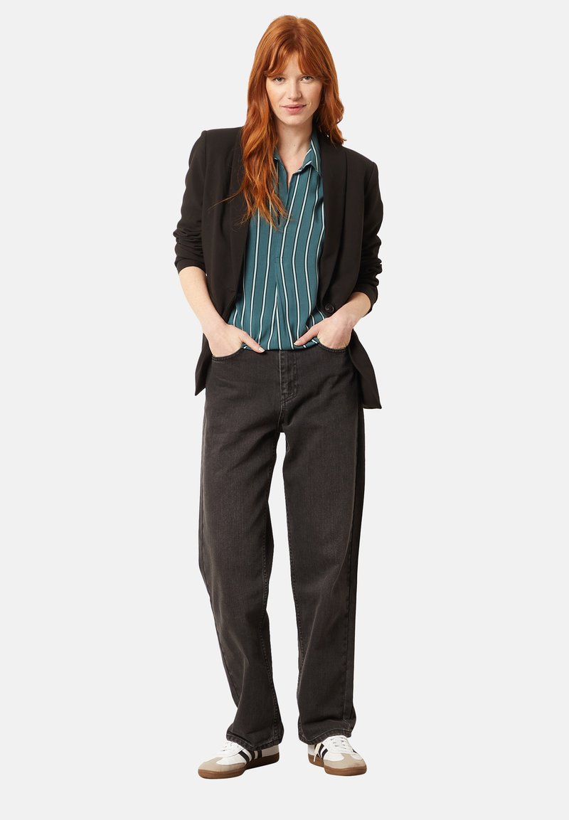 Blazer negro sobre una camisa de rayas teal, combinado con jeans oscuros holgados y zapatillas blancas con detalles en negro. Ajuste y diseño simple y clásico.