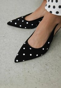 Ballerines noires à bout pointu avec des pois blancs et un design à décolleté bas. Texture de tissu lisse et fine bordure noire autour de l'ouverture.