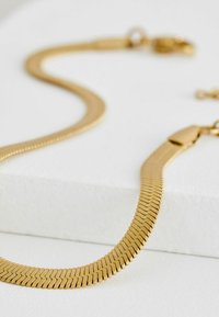 Collana in metallo dorato con un design piatto e flessibile, composta da segmenti rettangolari collegati. Presenta una chiusura a gancio per un indossamento sicuro.