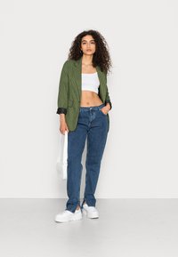 Blazer verde xadrez com acabamento preto, top cropped branco, jeans retos azuis e sapatilhas brancas de plataforma, segurando uma mala de ombro branca.
