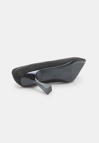 Pantofii cu toc înalt, negri, au un exterior texturat acoperit cu mărgele mici. Prezintă vârful ascuțit și un toc pătrat. Solea interioară este netedă.