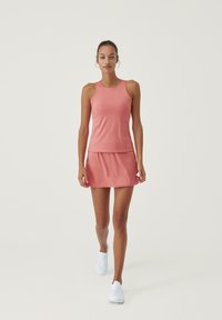 Träningslinne och kjolset i mjuk korall, med en åtsittande design och lätt tyg, parat med vita slip-on skor.