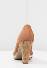 Chaussure à talon aiguille avec une tige en daim beige, un talon en liège et une surface texturée. Présente un bout arrondi et de subtils accents rayés à la base.