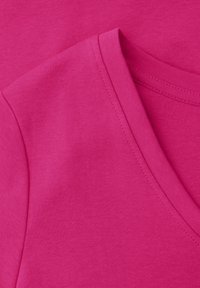 Zbliżenie na różowy, bawełniany T-shirt z krótkim rękawem, dekoltem w kształcie litery V oraz widocznymi przeszyciami na szwach i krawędziach.