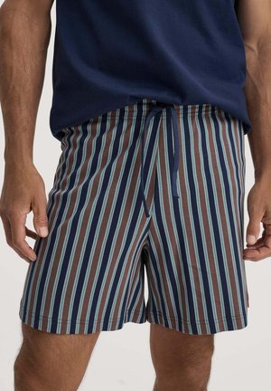 Mann trägt Shorts bis zur Mitte des Oberschenkels mit vertikalen braunen, marineblauen und hellblauen Streifen und einem marineblauen Kordelzug, kombiniert mit einem marineblauen Hemd.