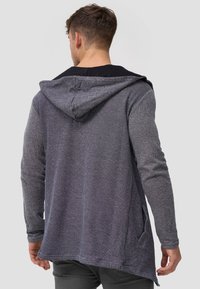 Grauer Hoodie mit langen Ärmeln aus strukturiertem Stoff, mit Kapuze und seitlichen Taschen, hinten länger geschnitten für eine lässige Passform.