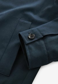 Tume tumesinine kangas sileda tekstuuriga, millel on silmapaistev nööbikas detail varruka ääres ja puhas, kohandatud disain.