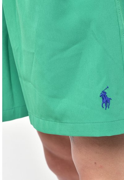 Pantaloni corti verdi realizzati in tessuto leggero, con un logo ricamato blu all'orlo e cuciture pulite lungo i bordi.