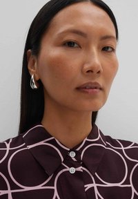 Silver teardrop earring, dark purple blouse with pink circular pattern, smooth texture, pointed collar, and two-button closure.