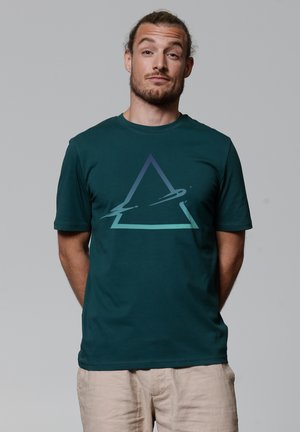Türkisfarbene Kurzarm-T-Shirts aus Baumwolle mit einem grafischen Gradienten-Dreieck und glatter Textur, getragen mit hellen Hosen.