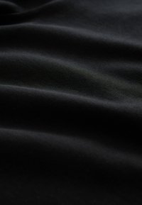 Fekete szövet sima textúrával, lágy redőkkel és finom fényléssel, kiemelve a hajtásokat és kontúrokat.