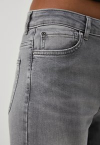 Primo piano di jeans di denim grigio che mostrano la tasca frontale, il passante per la cintura e i dettagli di cucitura sull'anca e sulla vita di una persona.