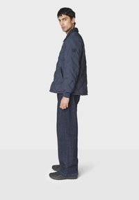 Mørkeblå quilted jakke med krave, sidelommer og ribbede manchetter, parret med mørke denimjeans og sorte strukturerede sneakers.