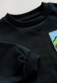 Felpa nera con polsini e colletto a costine. Presenta una toppa grafica con un design paesaggistico colorato sul davanti. Tessuto morbido.