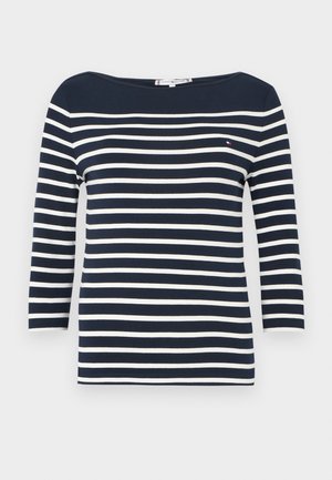 Chemise à manches longues bleu marine et blanc à rayures horizontales, col bateau et petit logo sur la poitrine gauche.