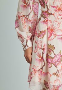 Vestido floral con una tela ligera y vaporosa que presenta patrones florales en rosa y verde. Mangas largas y abullonadas con detalles en los puños y un diseño fluido.