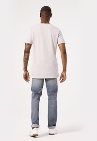 Lichtgrijs textuur T-shirt met korte mouwen, gecombineerd met lichtblauwe jeans en witte sneakers, gezien vanuit de achterkant.