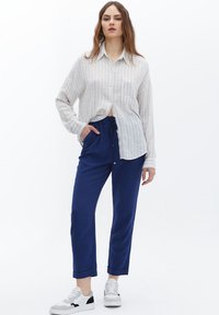 Witte gestreepte overhemd met knopen, gecombineerd met blauwe broek met trekkoord en witte sneakers met zwarte accenten. Losse pasvorm en gestructureerde stof.