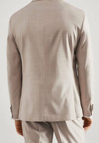 Lichtbeige colbert met een subtiel geruit patroon, getailleerde pasvorm, lange mouwen en knoopaccenten aan de manchetten. Zichtbare stiksel details.