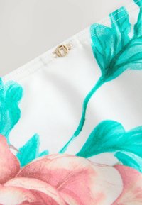 Bloemrijke stof in het wit met roze en teal bloemen. Kenmerkt een decoratieve gouden hardware-accent op de naad. Gladde textuur.