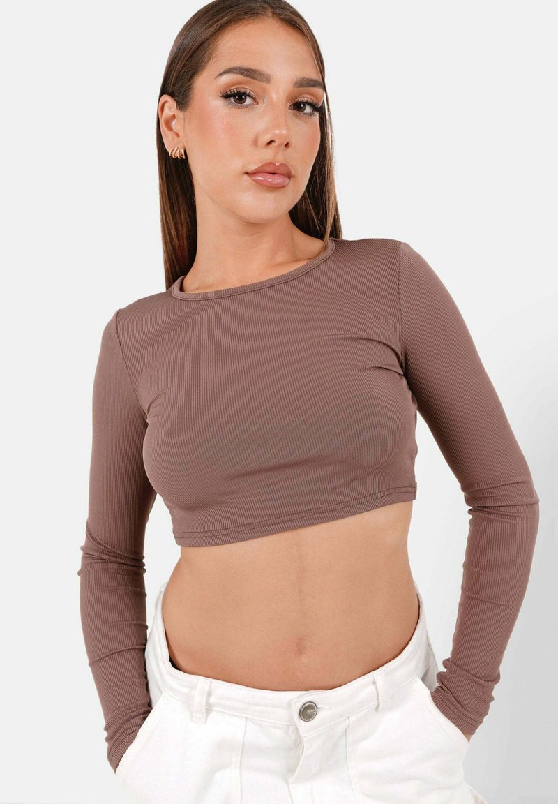 Braunes, geripptes Langarm-Crop-Top mit rundem Ausschnitt und figurnaher Passform, kombiniert mit hoch taillierten weißen Hosen.