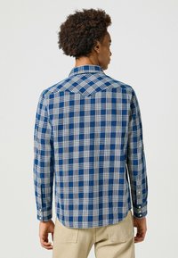 Camisa de manga larga de cuadros azules y blancos con un yugo puntiagudo, puños con botón y dobladillo curvado. Fabricada en un tejido texturizado.