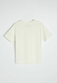 Jasna kremowa koszulka z okrągłym dekoltem i krótkimi rękawami, z teksturowanym prostokątnym naszywką na górnej części pleców. Wykonana z miękkiej bawełny.