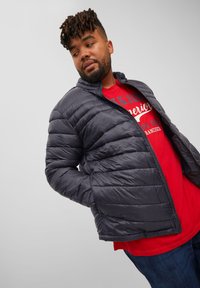 Chaqueta acolchada de color azul marino oscuro con diseño acolchado, cuello alto y cremallera frontal, llevada sobre una camisa roja brillante. Textura de tela suave y ligera.