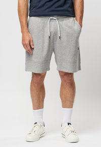 Shorts en coton gris avec taille élastique et cordon de serrage, poches latérales et un petit logo sur le côté. Associés à des baskets blanches et des chaussettes.
