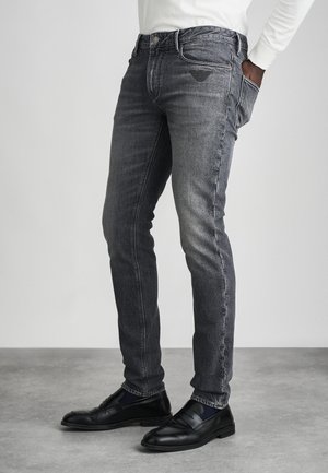 Jeans ajustados de color gris oscuro con un ligero desgaste, diseño de cinco bolsillos, logo bordado en el bolsillo trasero, combinados con mocasines negros.
