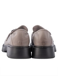 Beige leren schoenen met een afgeronde achterkant, een gestructureerde zwarte buitenzool en subtiele stikselaccenten langs de naden. Ontworpen voor comfort.