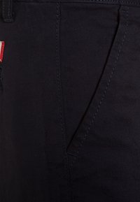 Pantaloni in denim blu scuro con vestibilità slim, tasche laterali inclinate, cuciture visibili e un piccolo etichetta rossa in vita.