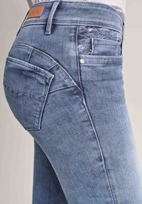 Světle modré denimové džíny s mírně opotřebovaným designem kapes, kontrastním prošíváním a koženou značkou na pase.