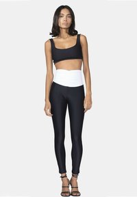 Top corto nero abbinato a leggings a vita alta con una fascia arricciata bianca. Tessuto liscio e elastico, e tacchi neri con cinghie.
