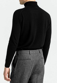 Schwarzer Rollkragenpullover mit geripptem Kragen, schmaler Schnitt, getragen mit grauen Wollhosen mit Gesäßtaschen und einem maßgeschneiderten Look.