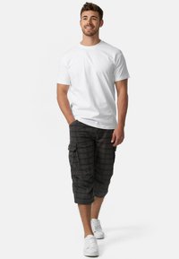T-shirt blanc à col rond associé à un short cargo à carreaux foncés avec des poches latérales, et portant des baskets blanches. Look décontracté et style relax.